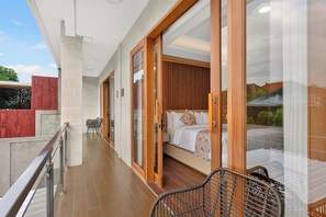 A balcony with a wooden railing, a bed with a wooden headboard, and a view of the surrounding area. - The Radiance Villas Seminyak (Badung)
