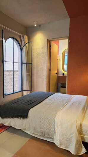 A bedroom with a bed, a window with curtains, a door leading to a bathroom, and a small mirror. - Loft Chic 2 Niveles Red Descanso Rooftop Grill Catedral Santuario S3 (Guadalajara)