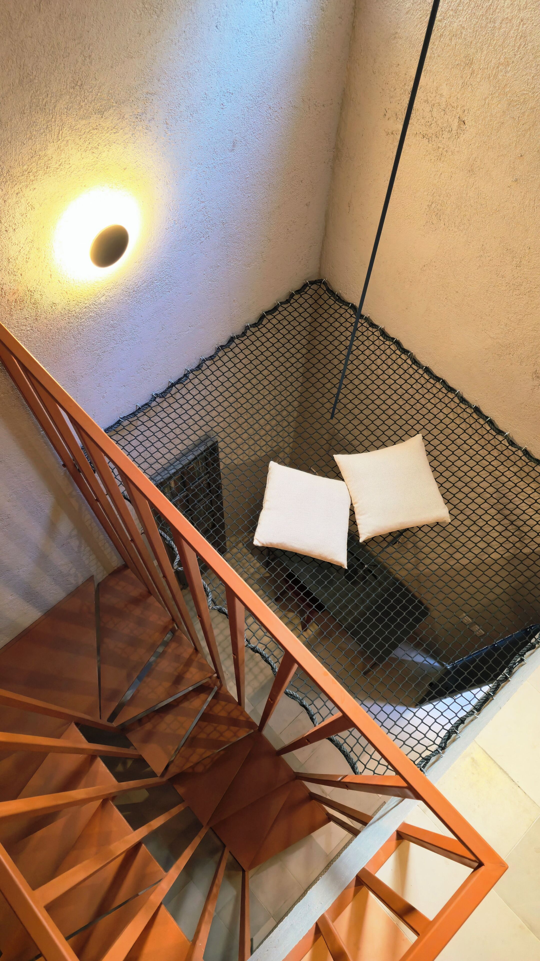 A corner of a room with a mesh partition, a wooden staircase, and a wall-mounted light fixture.