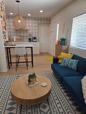 A modern living room with a blue sofa, a round wooden coffee table, and a kitchen area with a patterned backsplash. - Private beautiful modern 400 sq ft studio located in a quiet neighborhood in SCW (Sun City West)