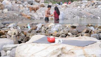 A rocky riverbank with a red teapot and a mug on a mat.