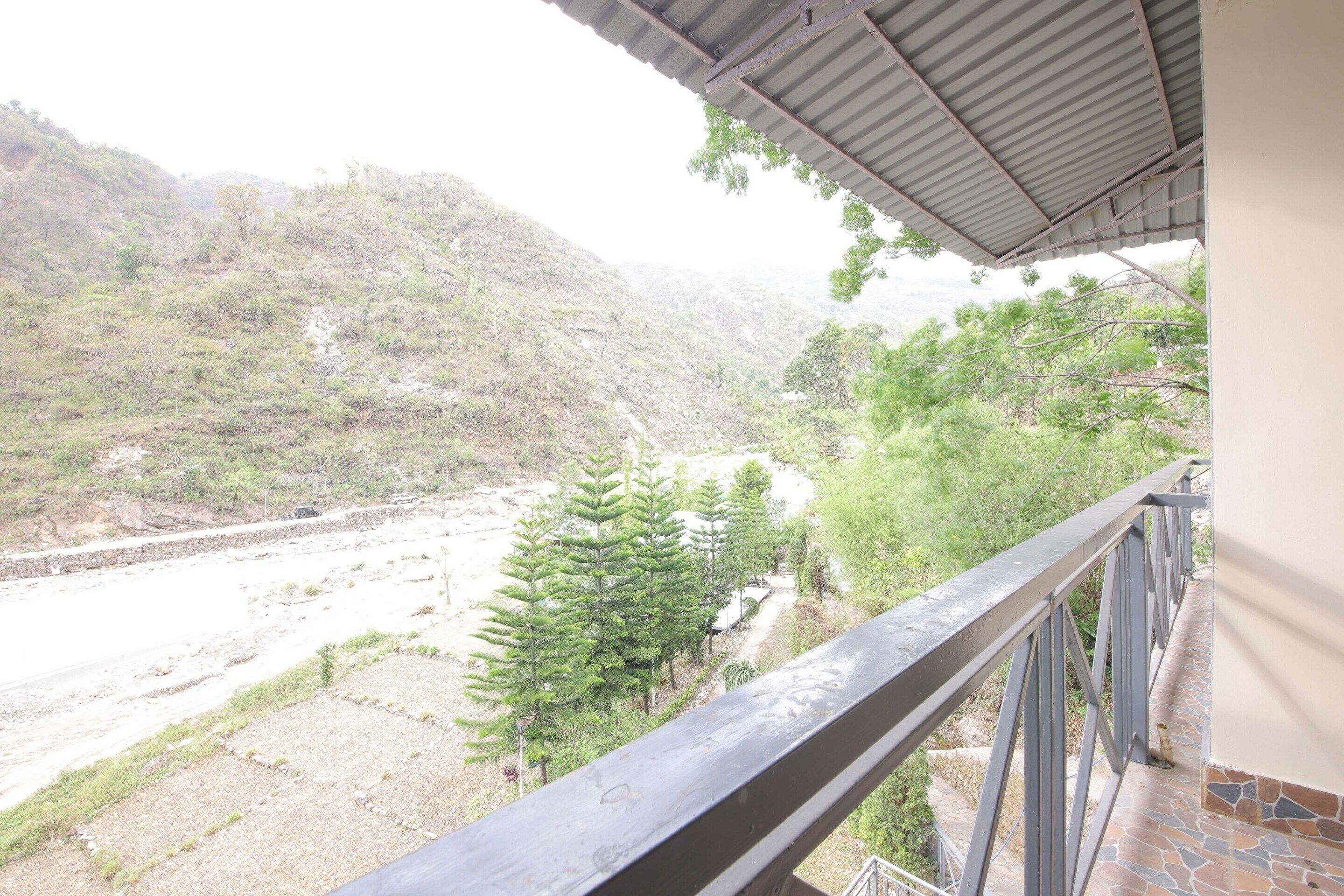 A balcony with a metal railing overlooking a river and hills.