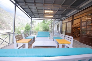 A covered outdoor seating area with white and blue furniture, a view of a mountainous landscape, and a wooden door with a lion statue. - Signature Suite With Hill and River Viewhotel Ribera (Dehradun)