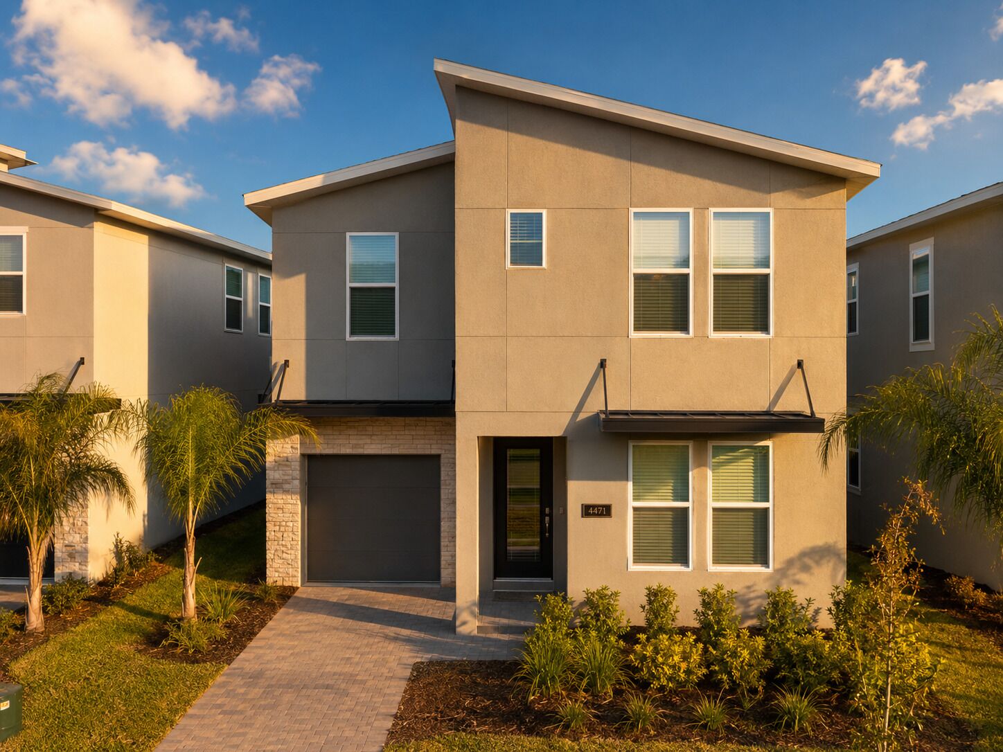 A modern two-story residential building with a brick entrance, a garage, and a well-maintained garden.