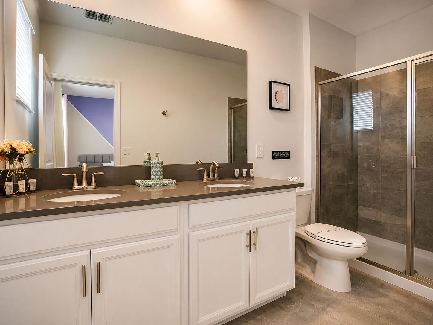 Een moderne badkamer met een wastafelmeubel met dubbele wastafel, een grote spiegel, een toilet en een douchecabine met glazen wanden.