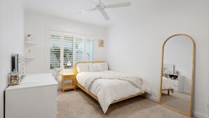Ein Schlafzimmer mit Bett, Nachttisch, Lampe, Spiegel und Deckenventilator.
