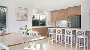 Eine moderne Küche mit Holzschränken, einem Edelstahlkühlschrank und einem Essbereich mit weißen Stühlen und einem Holztisch.