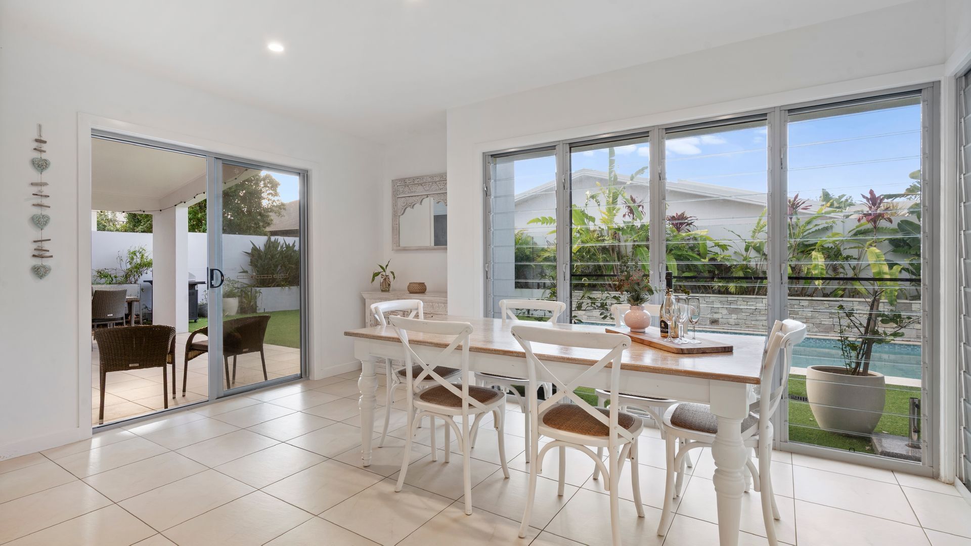 A modern dining area with a large window, white chairs, and a wooden table.