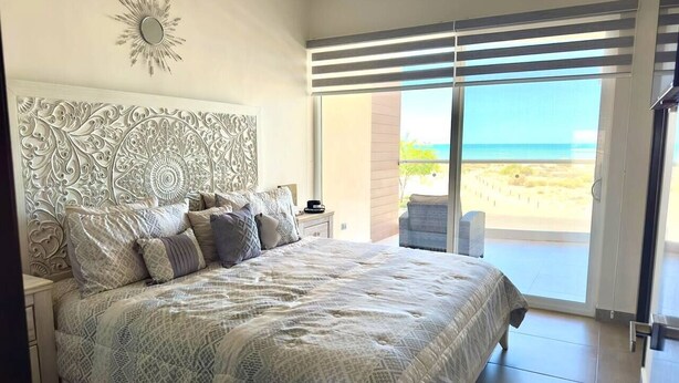 Ein Schlafzimmer mit Bett, Nachttisch, Stuhl und Blick auf den Strand.