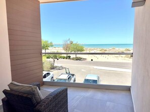 Un balcón con mobiliario de mimbre, vista a la playa y coches aparcados.