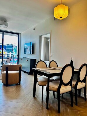Un soggiorno moderno con tavolo da pranzo, sedie, divano, televisore e una grande finestra vista città.