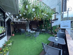 An outdoor seating area with tables and chairs, a sign indicating a hotel parking lot, and hanging planters with greenery.