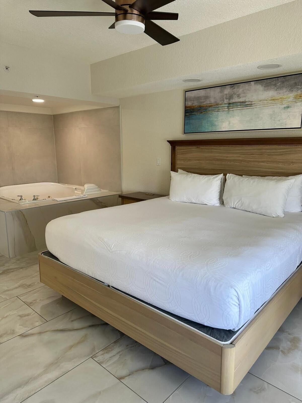 Habitación de hotel con una cama grande, ventilador de techo, un cuadro en la pared y una bañera.