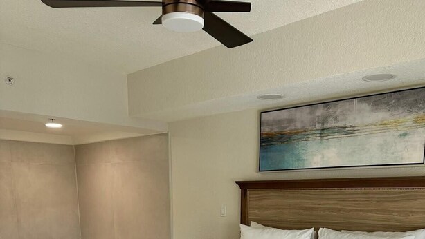 Une chambre d’hôtel avec un grand lit, un ventilateur de plafond, un tableau au mur et une baignoire.