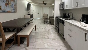 Une cuisine moderne avec des meubles blancs, un coin repas avec une table et des bancs en bois, et un salon avec un canapé et un téléviseur.