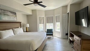 Une chambre à coucher avec un lit, un bureau, une télévision et un ventilateur de plafond.