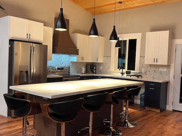 A modern kitchen with a central island, bar stools, stainless steel appliances, and pendant lighting.