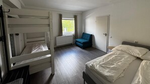 Huoneessa on kerrossänky, yksi erillinen sänky, tuoli, patteri ja ovi.