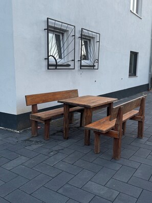 Un conjunto de banco y mesa de madera frente a un edificio blanco con una ventana y una puerta pequeña.