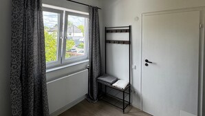 Huoneessa on ikkuna, kattotuuletin, ovi ja metallihylly.