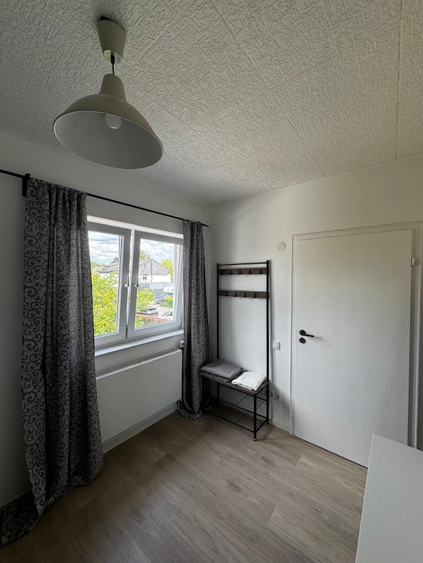 A room with a window, a ceiling fan, a door, and a metal shelf. - Guesthouse Cologne North For business travelers, tourists & families (Köln)