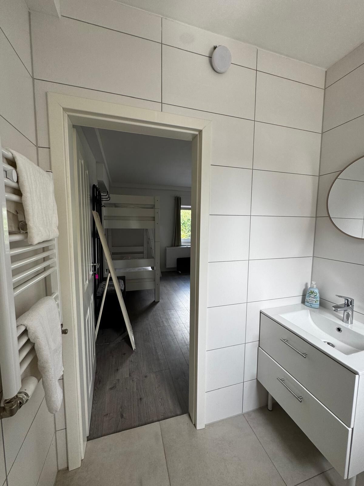 Un bagno rivestito di piastrelle bianche, con lavandino e specchio.