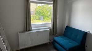 Huoneessa on ikkuna, patteri, sininen sohva ja valkoinen patteri.