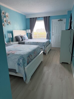 Un dormitorio con dos camas, una puerta blanca, un armario y vistas al balcón.