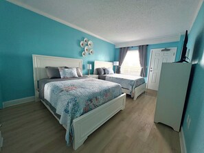 A bedroom with two beds, a dresser, a window with curtains, and a ceiling fan. - Cozy Soundside Retreat at Villas of Hatteras Landing (Hatteras)