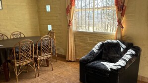 A room with a dining table, chairs, a sofa, and a window with curtains. - Nuestras Raíces Cabins (Las Vegas)