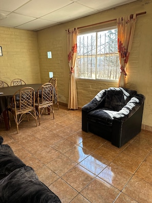 A room with a dining table, chairs, a sofa, and a window with curtains.