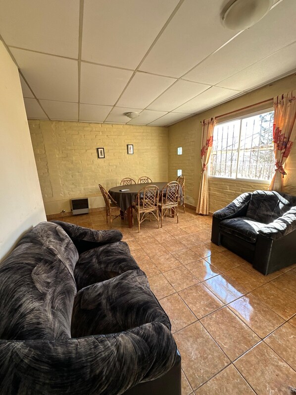 A living room with a sofa, a dining table with chairs, a window with curtains, and a brick wall.