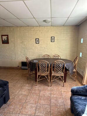 A room with a round table, four wicker chairs, a black tablecloth, a tiled floor, and a brick wall.