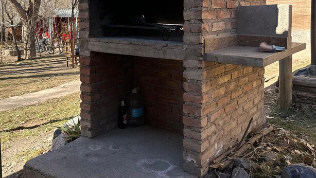A brick-built outdoor oven with a chimney, surrounded by a grassy area and a building in the background. - Nuestras Raíces Cabins (Las Vegas)