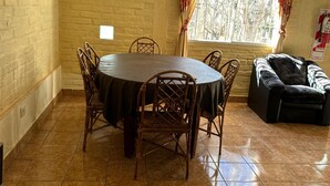 A dining area with a round table, chairs, a sofa, and a window with curtains. - Nuestras Raíces Cabins (Las Vegas)