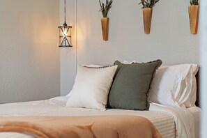 Un lit bien fait, avec des oreillers, un luminaire suspendu et deux jardinières fixées au mur.