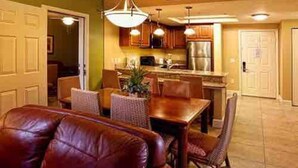 A living room with a brown leather sofa, a dining table with chairs, and a kitchen area with cabinets and appliances. - Westgate Lake 2 Bed in Orlando close to Disney (Orlando)