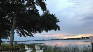 Two white Adirondack chairs facing a calm lake with a sunset view, a warning sign, and a tree to the left. - Westgate Lake 2 Bed in Orlando close to Disney (Orlando)