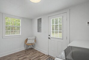 Ein Zimmer mit einer Tür, zwei Fenstern, einem Korbstuhl und einem weißen Schrank.