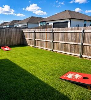 Un patio con césped artificial, dos blancos de disc golf rojos, una valla de madera y casas al fondo.