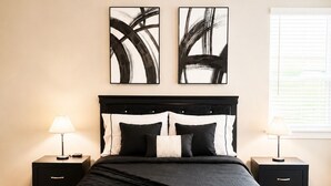 Ein Schlafzimmer mit einem großen Bett, zwei Nachttischen, einem Deckenventilator und abstrakter Kunst an der Wand.