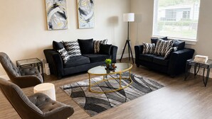 Ein modernes Wohnzimmer mit zwei schwarzen Sofas, einem Glastisch und einer Stehlampe.