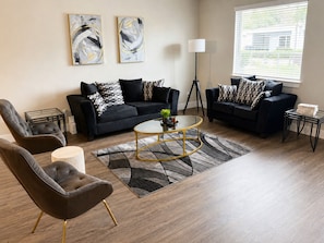 A modern living room with two black sofas, a glass coffee table, and a floor lamp.