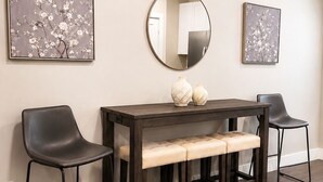 Ein Essbereich mit einem dunklen Holztisch, zwei schwarzen Stühlen, einer Bank und zwei an der Wand hängenden Bildern.