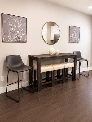 Un comedor con una mesa de madera oscura, dos sillas negras, un banco y dos cuadros colgados en la pared.