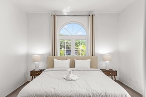 Ein Hotelzimmer mit einem großen Bett, zwei Nachttischen mit Lampen, einem Fenster mit Vorhängen und einem Handtuch auf dem Bett.