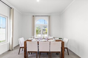 Ein Essbereich mit einem Holztisch, gedeckt für sechs Personen, weißen Stühlen und einem großen Fenster mit Vorhängen.