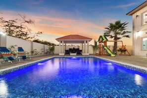 Ein Swimmingpool mit Gazebo, Liegestühlen und einer Rutsche.
