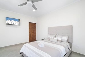 Um quarto com cama, ventilador de teto, porta e um quadro na parede.