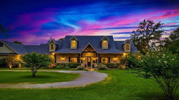 Une grande maison avec une pelouse bien entretenue, une allée et une véranda illuminée.
